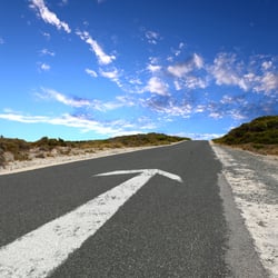 Empty countryside road with white arrow sing on it